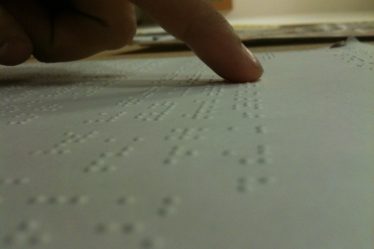 A finger follows the raised dots of Braille text