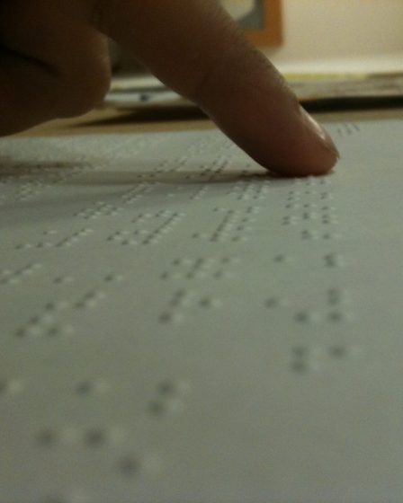A finger follows the raised dots of Braille text