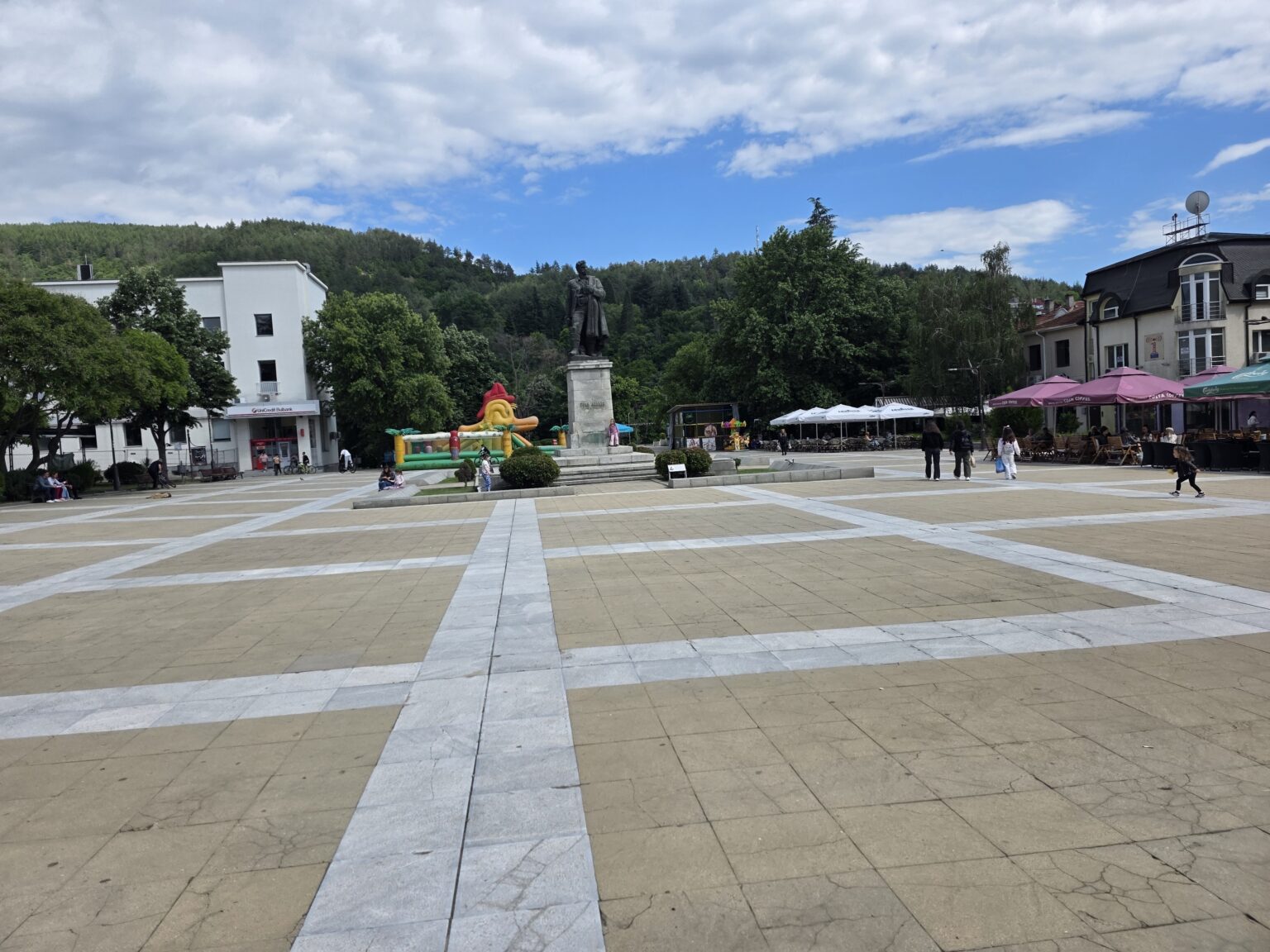 A broad square with a monument on a pedestal and a wooded hill behind it in Blagoevgrad
