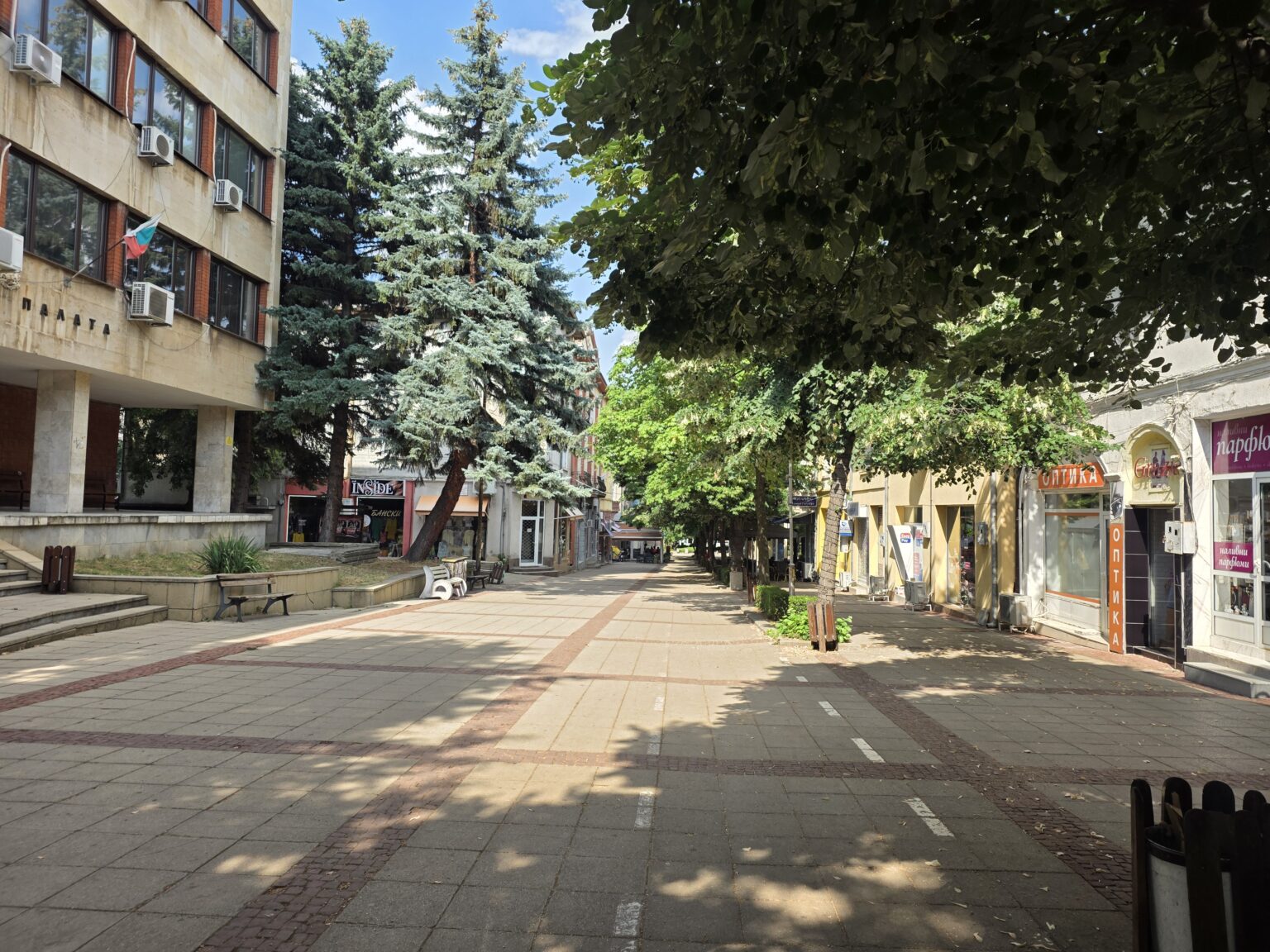 A pedestrian shopping street with small shops and an administrative building in Dupnitsa