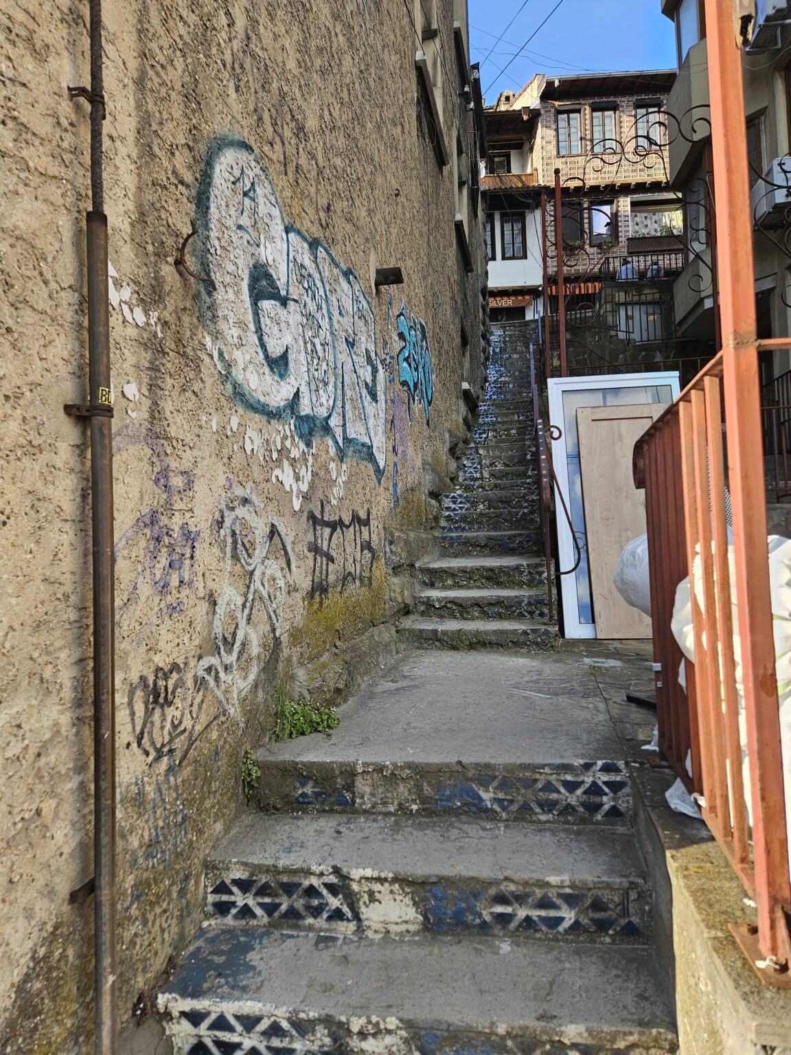 Narrow concrete stairway with blue and white tiles on the steps and graffiti on the wall, running between old houses
