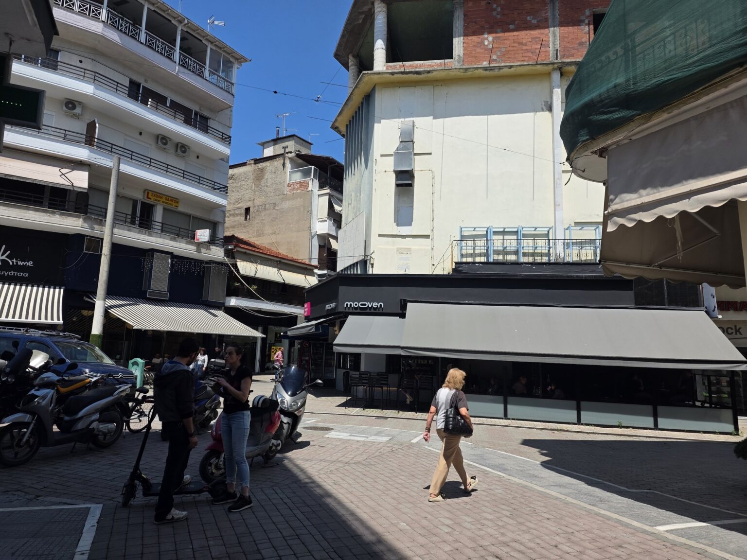 Pedestrians on a busy street with modern buildings and parked motorbikes