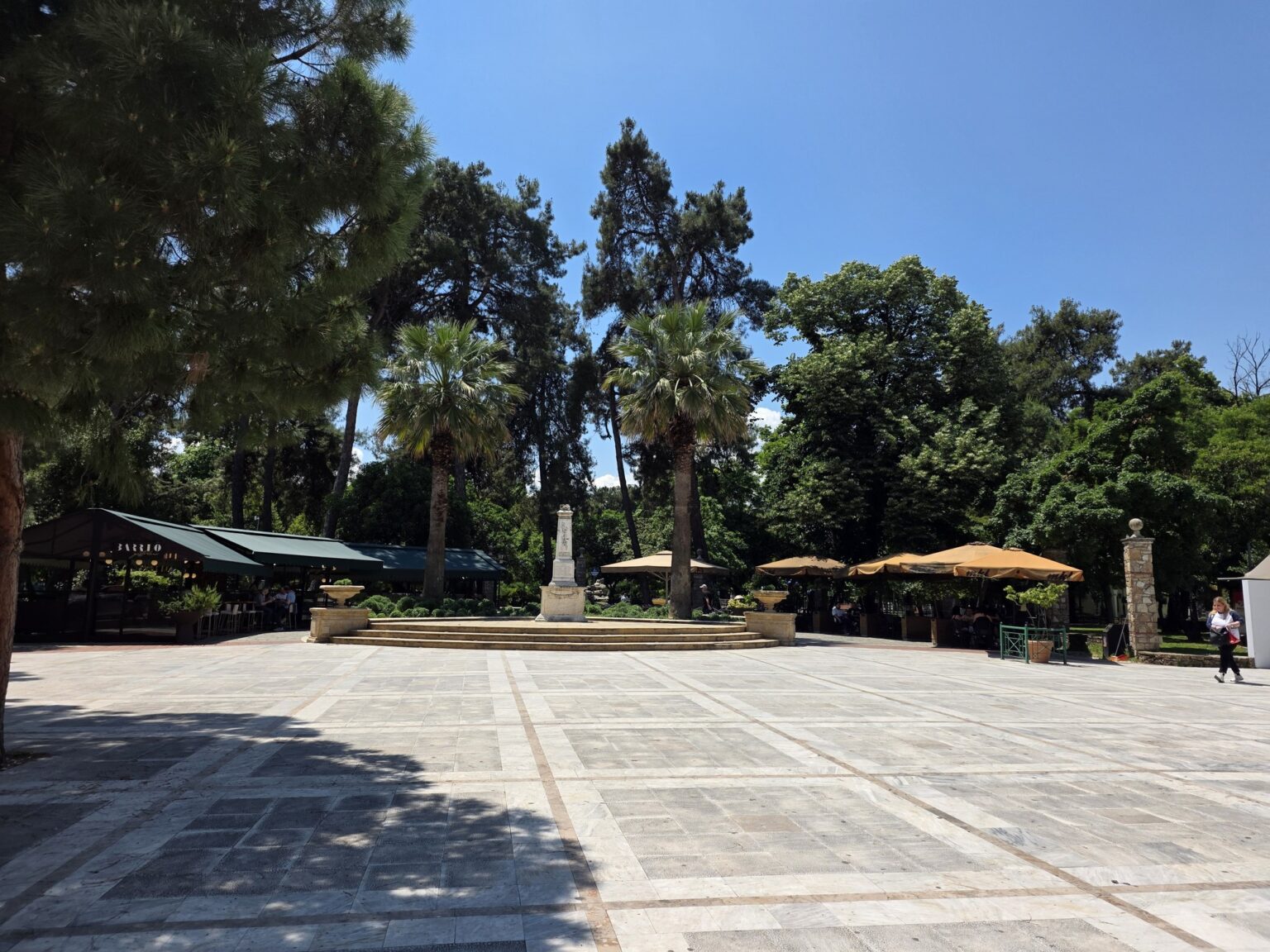 Square with tiles, trees and buildings under a clear blue sky