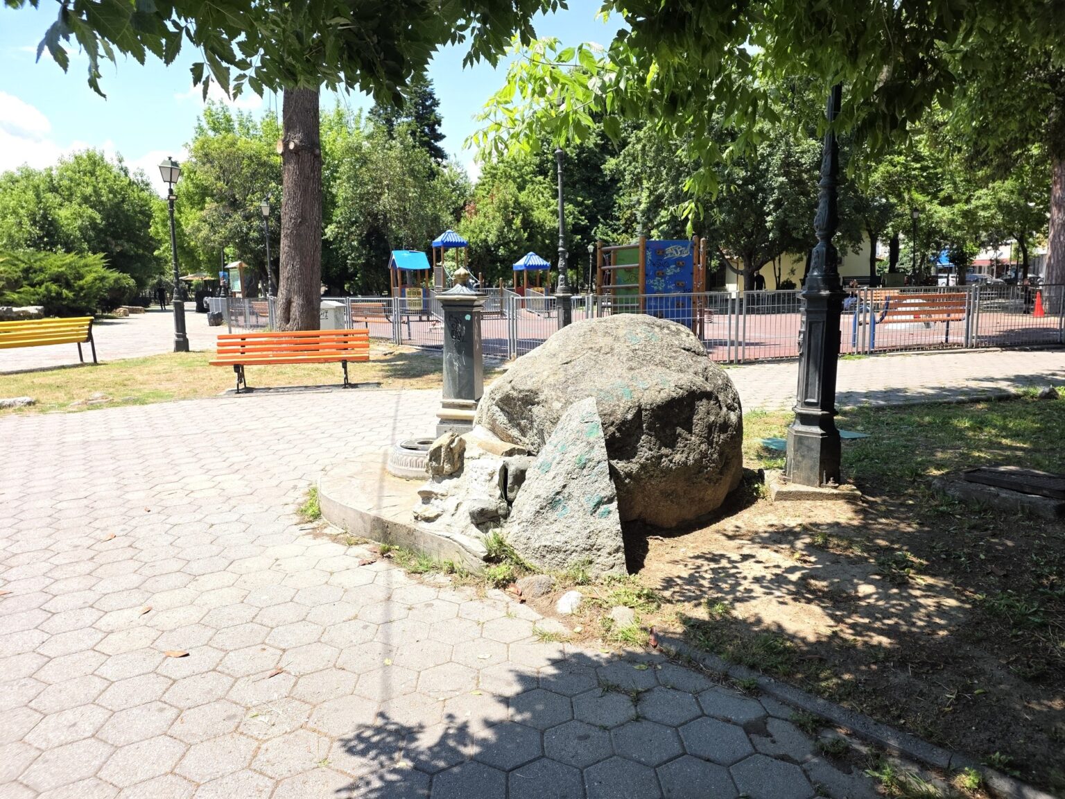 Large stone in the park among a pedestrian alley and green trees