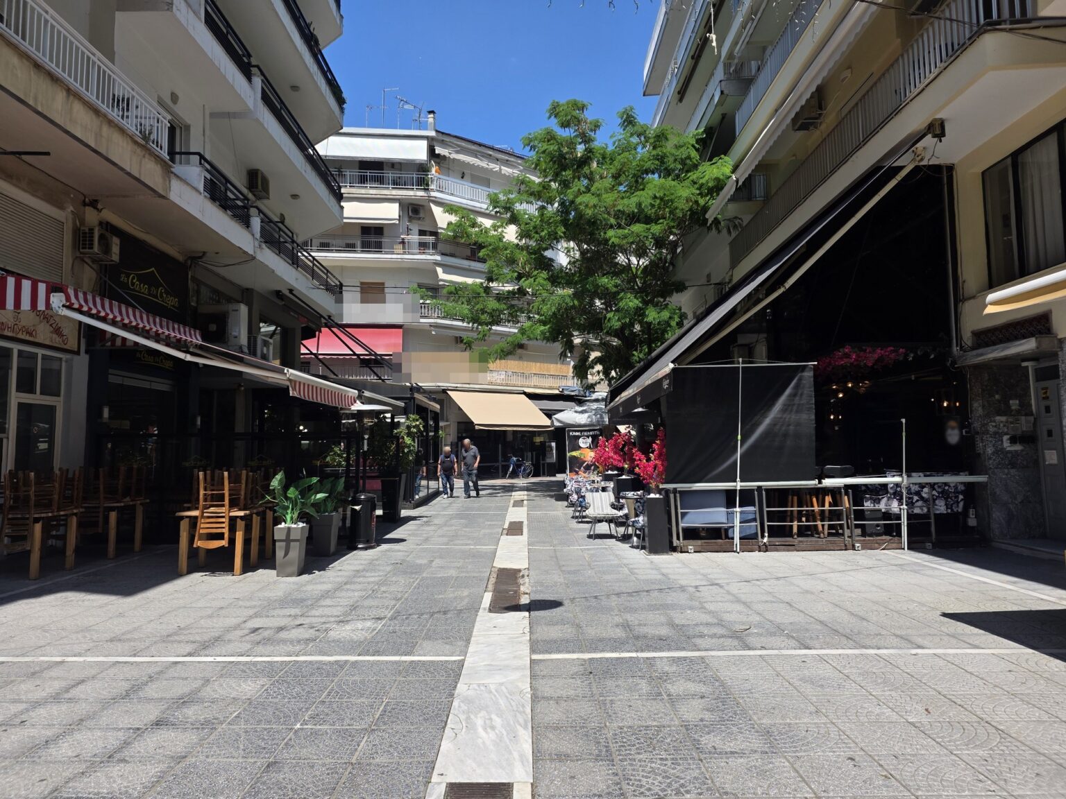 Pedestrian street with outdoor cafe tables and buildings with balconies