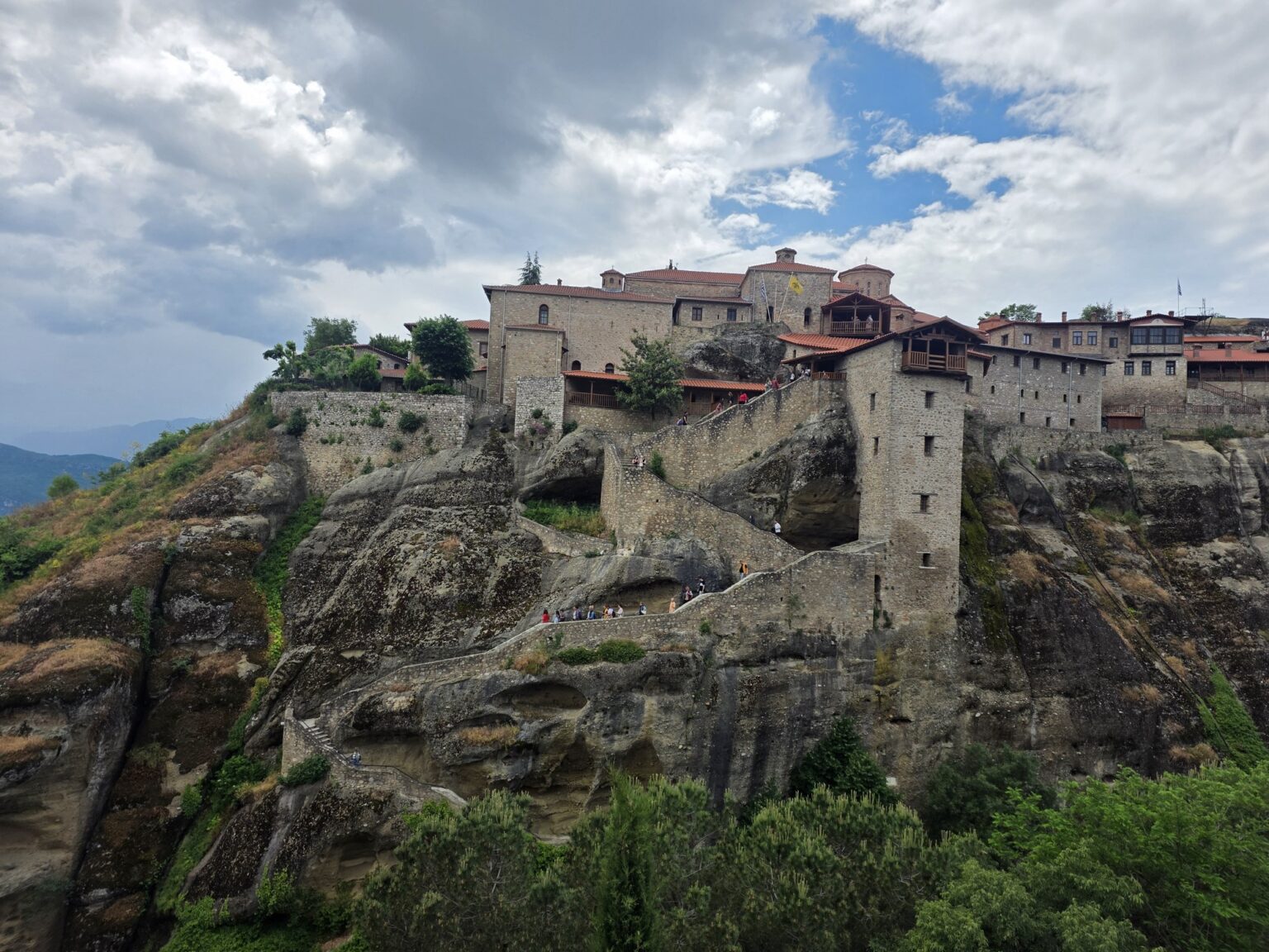 A monastery on a high rock formation with a cloudy sky above it