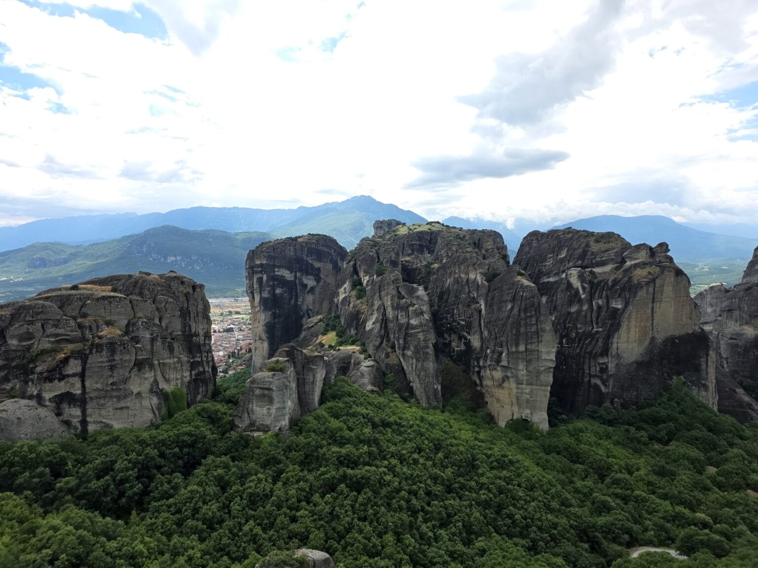 Massive rock formations amidst green forests and cloudy sky