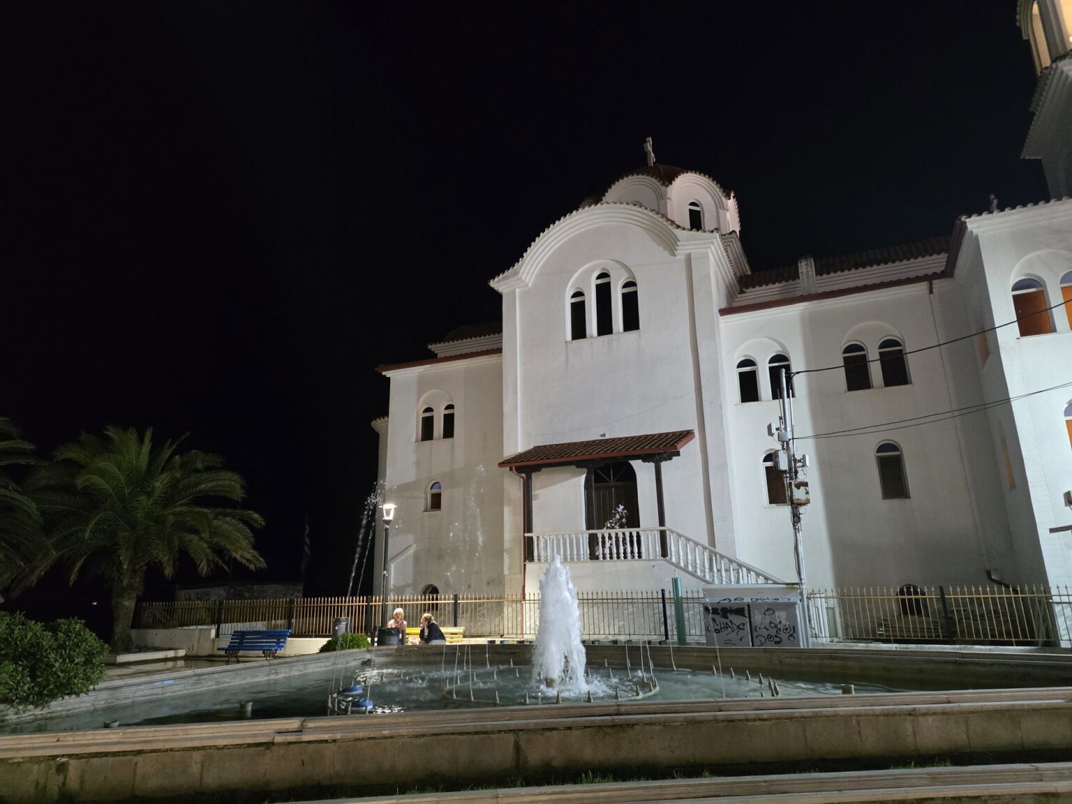 White church with domes at night and a fountain in front