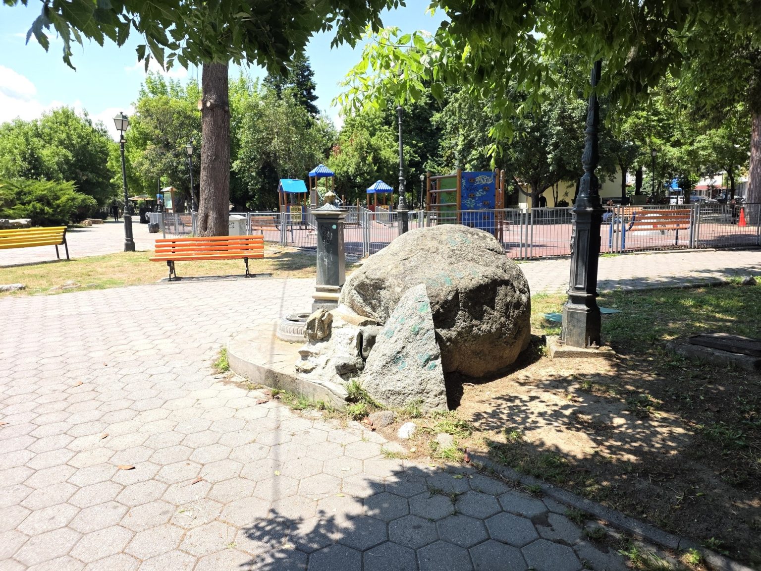 Голям камък в парка сред пешеходна алея и зелени дървета