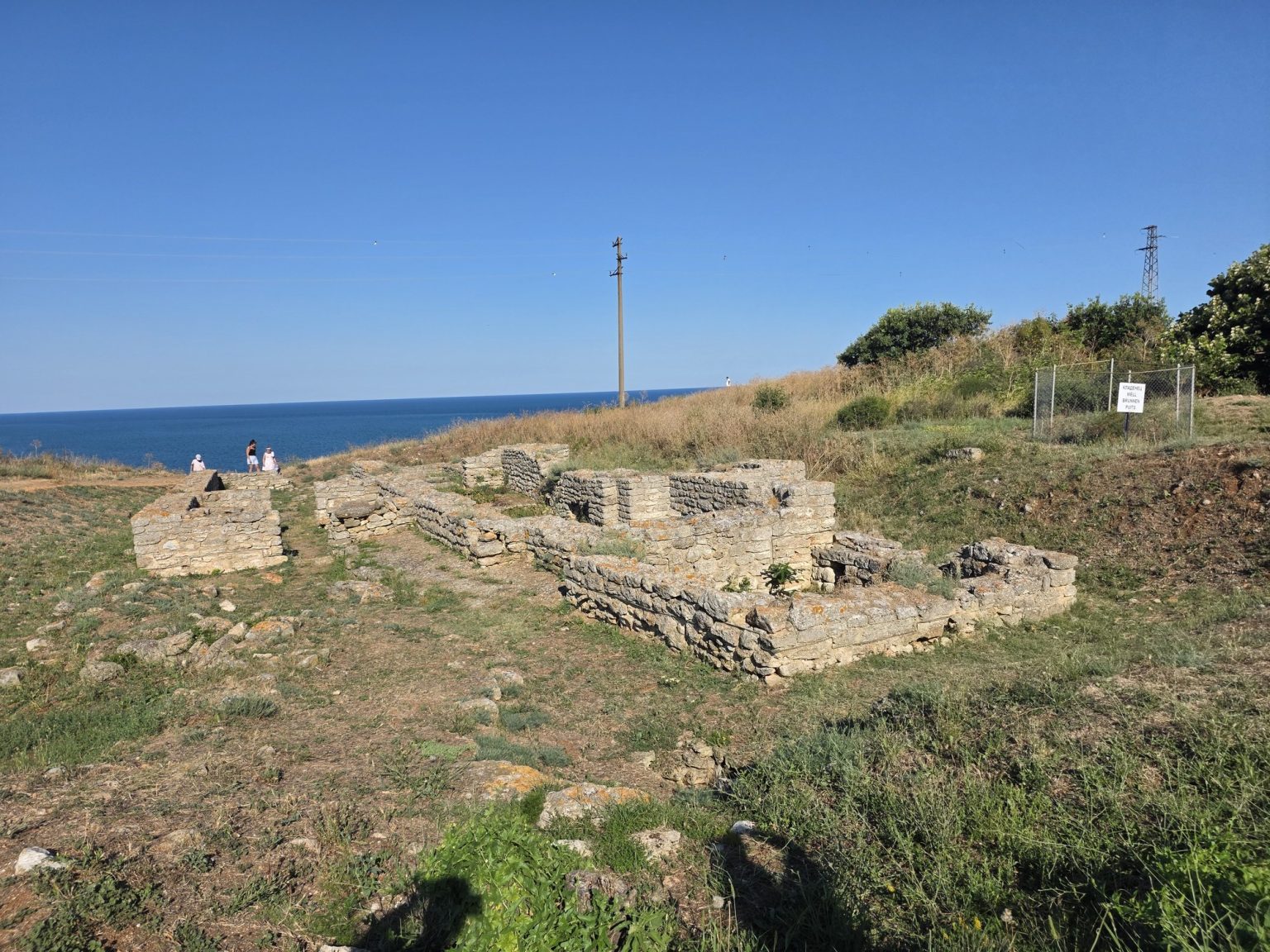 Ниски каменни останки от сгради и синьо море в далечината